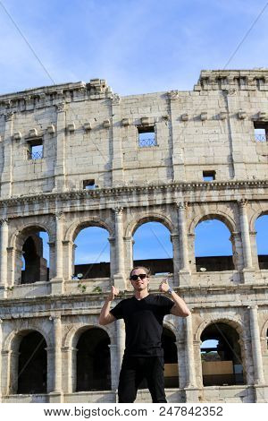 Boy In Glasses Wearing Black Clothes And Standing Near Coloseum In Background In Rome, Italy. Concep
