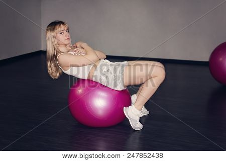 Blonde Girl Or Young Woman With Green Eyes And Red Lips Lying On  Pink Gymnastic Ball Looking Exhaus