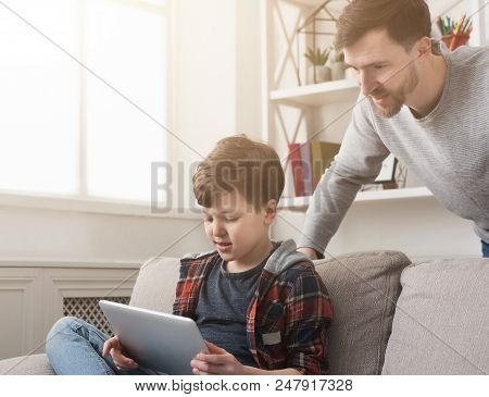 Father And Son Spending Time Together And Using Digital Tablet On Sofa At Home