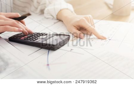 Female Hands With Calculator, Sheet And Graphs. Calculating New Project Budget And Analyzing Its Inv