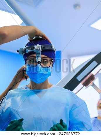 The Surgeon With A Magnifying Glass During Medical Surgery In The Operating Room. Assistant Helps Th