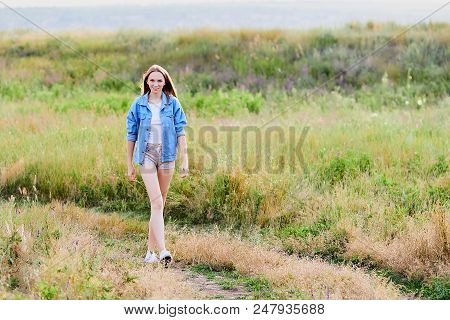 Happy Smiling Young Girl Wearing Blue Jeans Jacket And Shorts Is Standing In The Field