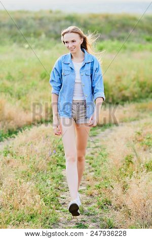 Happy Smiling Young Girl Wearing Blue Jeans Jacket And Shorts Is Standing In The Field