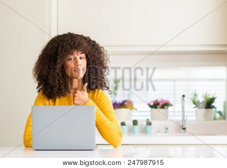 African american woman using computer laptop at kitchen happy with big smile doing ok sign, thumb up with fingers, excellent sign