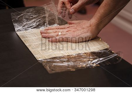 Chef Preparing Sushi Mat With Plastic Wrap To Make A Roll For A Cooking Class