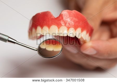 Denture prosthesis in doctor orthodentist dentist hand, checking with mirror