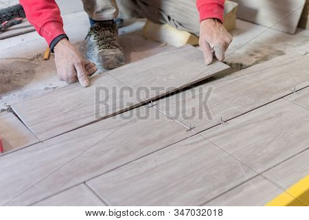 Man Installing Rectangular Shaped Floor Tiles In Kitchen. Applying Adhesive Before Installation And 