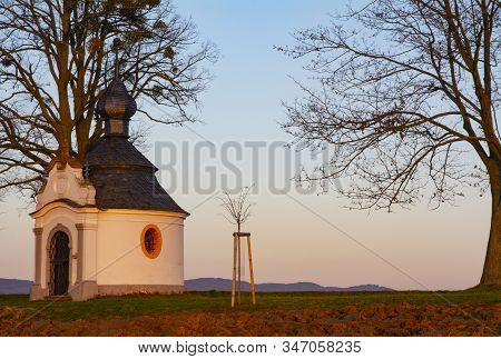 Chappel In Late Afternoon Sunshine With Trees And Field