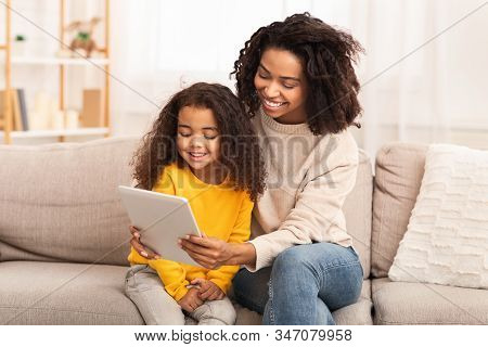 Cute Black Family Of Mother And Daughter Using Tablet Computer Watching Cartoons Together Sitting On