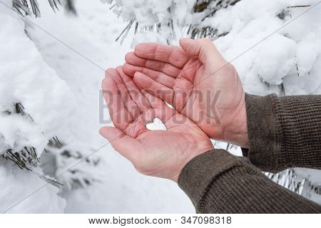 Mature man with chapped hands holding silver metal heart outside in winter