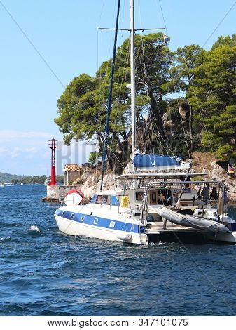 Sailing Catamaran Sails Along The Rocky Green Coast Past The Red Literary Sign - The Fairway Lightho