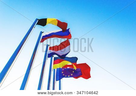 National Flags On Flagpoles. National Flags Of The Countries Are Flying In The Wind Against The Blue