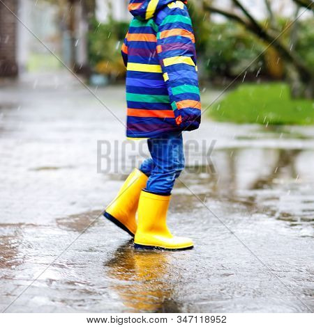 Close-up Of Kid Wearing Yellow Rain Boots And Walking During Sleet, Rain And Snow On Cold Day. Child