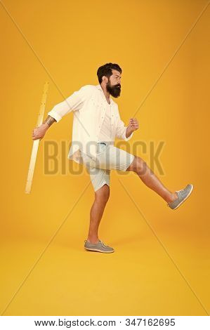 Knowledge In Brutal World. Brutal Hipster Walking With Ruler On Yellow Background. Bearded Man With 