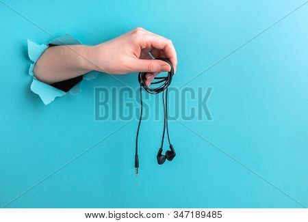 Headphones In A Womans Hand On A Blue Background With A Hole