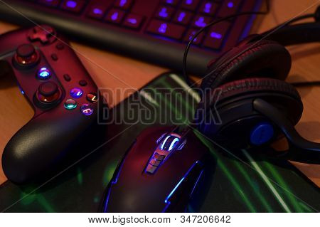 Modern Gamepad And Gaming Mouse Lies With Keyboard And Headphones On Table In Dark Playroom Scene. E