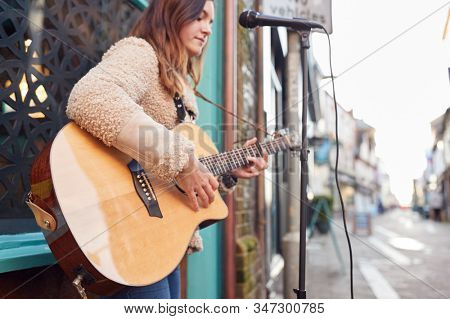 Female Musician Busking Playing Acoustic Guitar Outdoors In Street