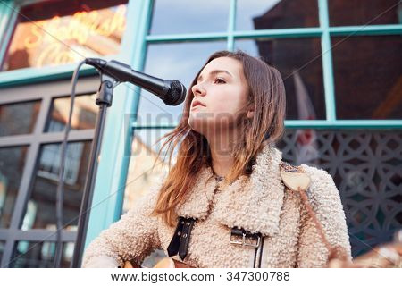 Female Musician Busking Playing Acoustic Guitar And Singing Outdoors In Street