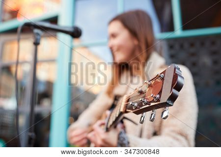 Focus On Guitar As Female Musician Busks And Sings Outdoors In Street
