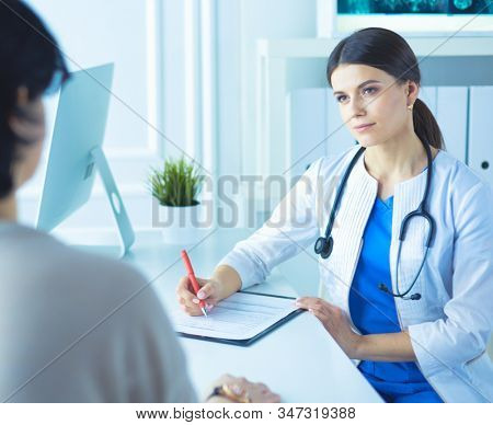 Doctor and patient discussing medical problems in a hospital consulting room. Doc filling in a patient's form