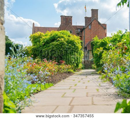 Slab Path Between Gardens And Trees Leading To Steps And House At End.