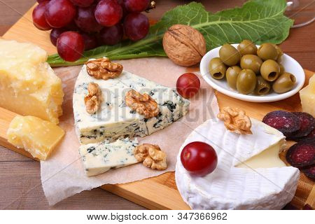 Assortment Of Cheese With Fruits, Grapes, Nuts, Glass With Wine And Cheese Knife On A Wooden Serving