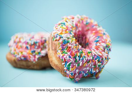 Two donuts with pink icing and candies on a blue pastel background