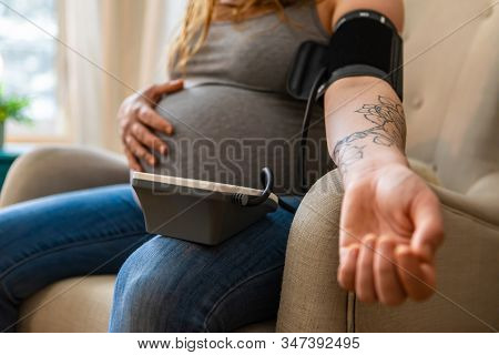 A Closeup Shot On The Tattooed Arm Of A Young Pregnant Woman Using A Digital Sphygmomanometer To Mea