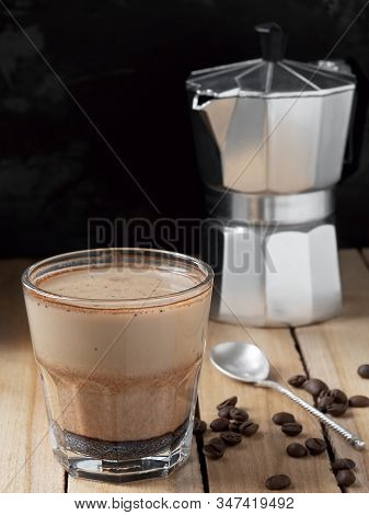 Coffee In A Glass With Cream And Coffee Beans On A Wooden Background. Near Moka Pot And Spoon. Close