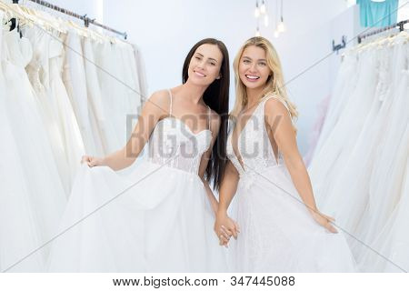 Portrait of happy attractive young brides in stylish wedding dresses standing in show room