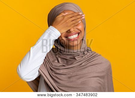 Facepalm. Cheerful Black Muslim Woman In Headscarf Covering Eyes With Hand And Laughing, Feeling Shy