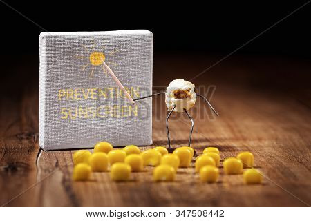 Funny Popcorn Figure Is Holding A Stick And Points To An Canvas, The Text Suncreen And Prevention On