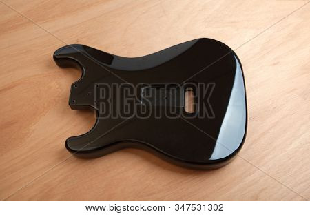 Black electric guitar body, back side on work bench.