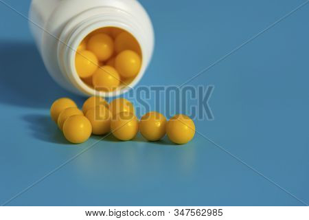 Yellow Vitamins Pour Out From A Pill Bubble On A Blue Background. Vitamin Complex. Multivitamins To 