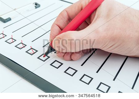 Close-up Of Hand Holding Red Pen Ticking Off Checklist Or To-do List On Clipboard