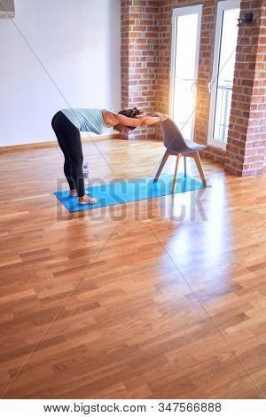 Middle age beautiful sportwoman standing on mat. Practicing yoga doing down dog on chair pose at gym
