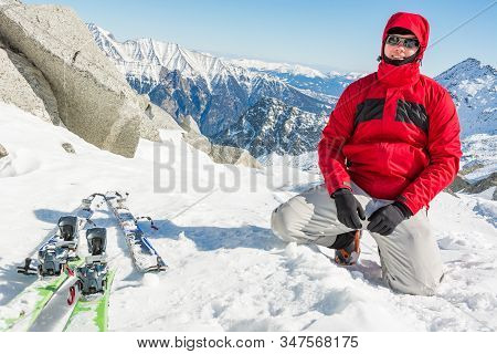 Male Ski Tourer Posing Next To Pair Of Skis In The Mountains.