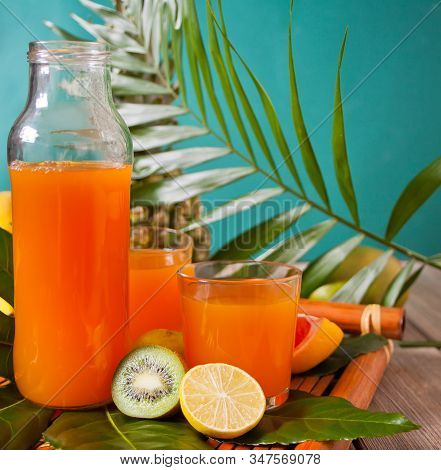 Glasses And Bottle Of Tropical Exotic Multifruit Juice With Pineapple And Palm Leaf On The Backgroun