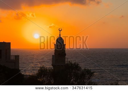 Round tower crowned with a crescent is a Muslim minaret. Old Yaffo - one of the most ancient cities of the world. The sun plunges into the Mediterranean Sea