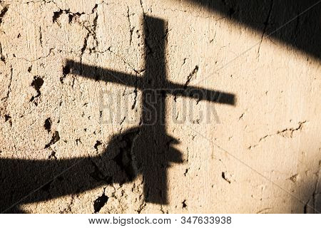 Shadow Of The Hand Holding A Christian Cross. Christian Symbol.