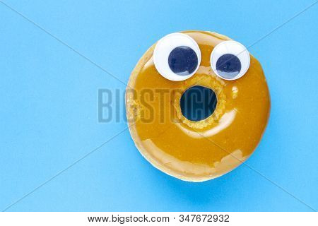 A Canadian Maple Dip Donut With Black Wiggle Googly Eyeballs On A Blue Background