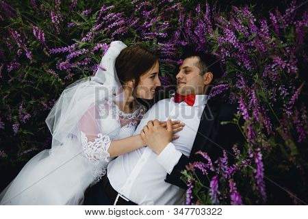 Couple At Sunset In A Wedding Dress Lie On The Grass With Lipin Flowers,festive Spring Wedding Photo