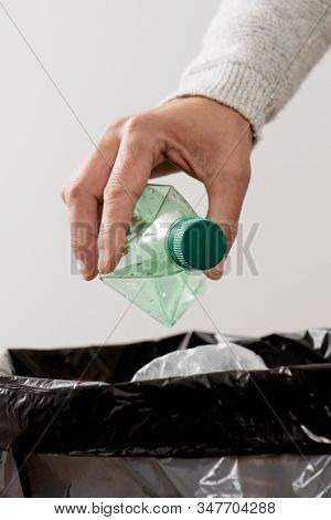 closeup of a young caucasian man about to throw an empty plastic bottle to the trash bin