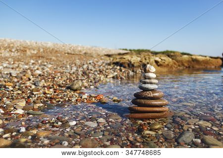Pyramid Of Stones For Meditation, Lying On The Sea Coast At Sunset. Stack Of Stones Against Blurred 