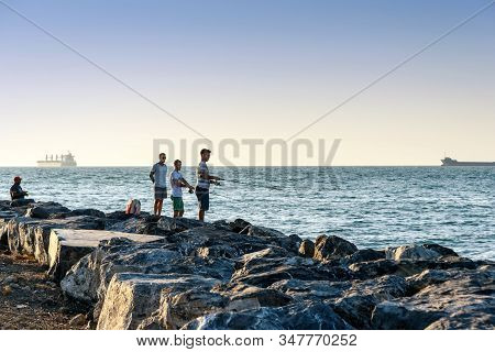 Iskenderun, Turkey - August 24, 2019: Sea Fishing On Spinning On The Stone At Seaside At Sunset. Men