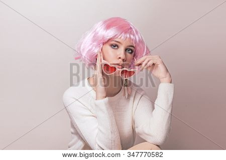 Portrait of teenage model with pink hair posing against pastel background. Studio photo of funky teenager wearing color wig and trendy glasses.