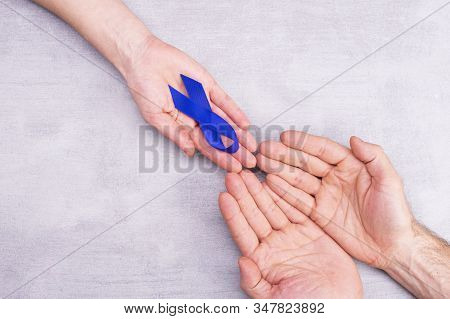 A Woman Holds Out A Blue Awareness Ribbon, Symbol In Male Hands, Colon Cancer, Colorectal Cancer On 