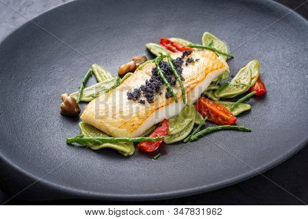 Gourmet fried Italian sea bass fish filet with spinach pasta, caviar and tomatoes as closeup on a modern design plate 