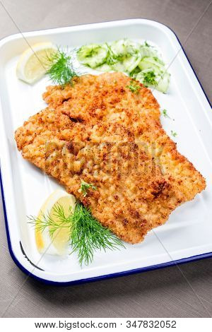 Traditional deep fried Wiener schnitzel from veal topside with cucumber salad and cranberry jam offered as closeup on a white tray
