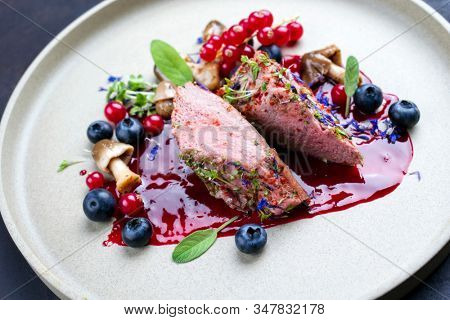 Fried dry aged venison tenderloin fillet medallion steak natural with mushrooms and forest berries as closeup on a modern design plate 